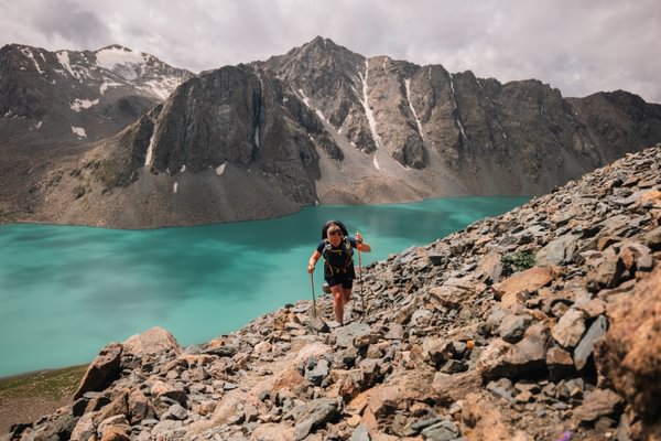 Runner ascending mountain terrain above a turquoise alpine lake