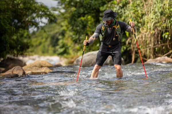 Runner crossing a jungle river with trekking poles