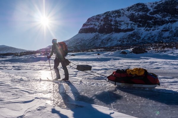 Explorer pulling a pulk across frozen terrain beneath mountain peaks